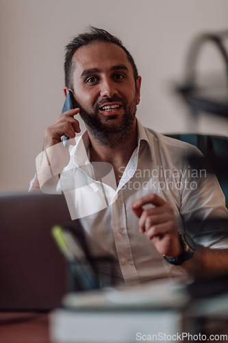 Image of A businessman talking on his smartphone while seated in an office, showcasing his professional demeanor and active communication.