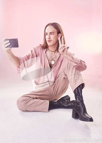Image of Selfie, peace and fashion with a gay man in studio on a pink background for lgbt inclusion or pride. Transgender, non binary and photograph with a male model sitting on the floor for trendy style