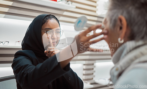 Image of Optometry, vision and eye test with an islamic woman optician working to diagnose a customer. Doctor, optometrist and eyecare with a muslim female testing a client for prescription lenses in a clinic
