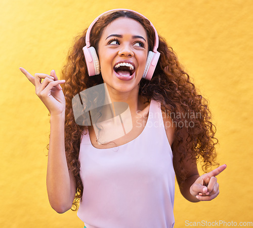 Image of Music, thinking and dance with a black woman listening to the radio outdoor on a yellow wall background. Headphones, energy and face with an attractive young female streaming audio sound for fun