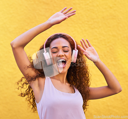 Image of Music, freedom and dance with a black woman listening to the radio outdoor on a yellow wall background. Headphones, energy and face with an attractive young female streaming audio sound for fun