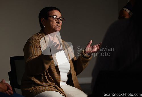 Image of Counselling, mental health and a senior woman talking for therapy, meeting or psychology in a dark room. Patient, psychologist or therapist talking in group workshop, consultation or rehabilitation