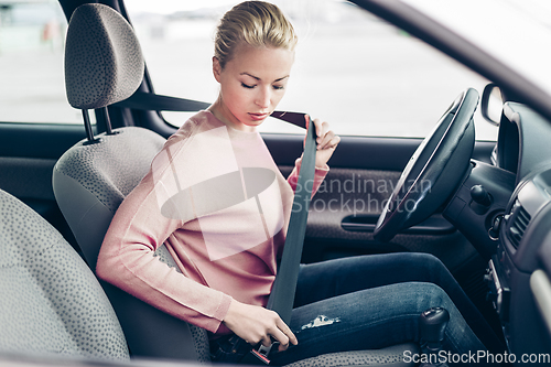 Image of Beautiful woman fastening seat belt in small personal car.