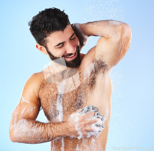 Image of Shower, cleaning and man with sponge, soap and water splash in studio for wellness, hygiene and grooming. Skincare, health and happy male with foam, cosmetics and washing body on blue background