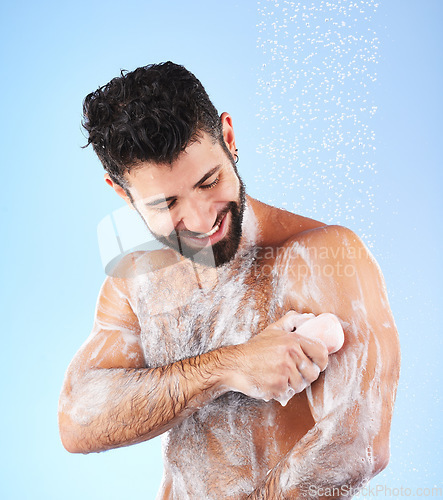 Image of Soap, shower and man with water splash, smile and hygiene in studio for wellness, cleaning and grooming. Skincare, healthy skin and happy male with foam, cosmetics and washing body on blue background