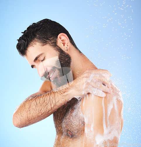 Image of Shower, cleaning and man with water, smile and soap in studio for wellness, hygiene and grooming. Skincare, healthy skin and happy male with foam, bath cosmetics and washing body on blue background