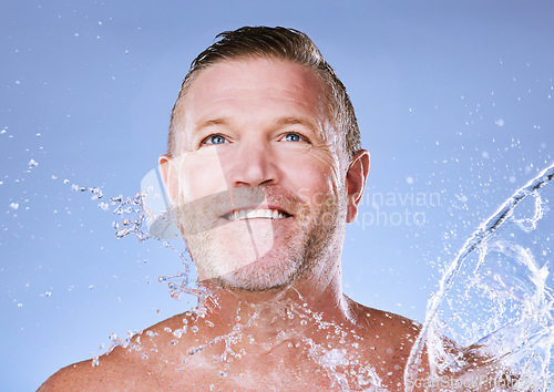 Image of Wellness, water splash and senior man cleaning, morning routine and washing on blue studio background. Male, mature gentleman and daily hygiene with clear liquid for dermatology, skincare or grooming