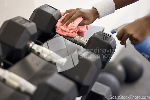 Image of Dumbbells, cleaner and hands cleaning at a gym with liquid soap in spray bottle with cloth for wellness. Janitor or person wipes dirty bacteria on dusty weights, tools or fitness training equipment