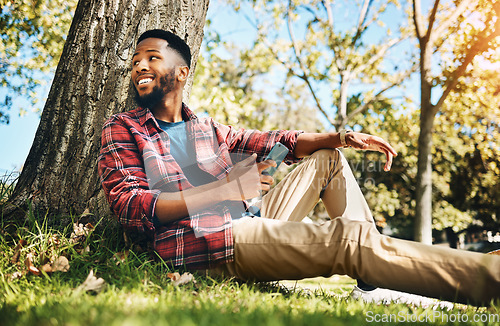 Image of Nature, phone and man sitting by a tree in an outdoor park networking on social media or the internet. Technology, rest and African guy browsing on mobile app with cellphone while relaxing in garden.