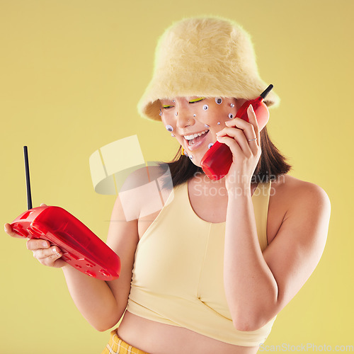 Image of Woman, landline phone call and studio background for yellow fashion, excited and smile with eyes sticker art on face. Asian gen z model, 90s aesthetic and telephone communication, talk or happy chat