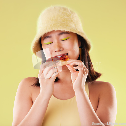 Image of Asian girl, eating pizza and studio with fashion, happiness and retro 90s aesthetic by yellow background. Young gen z model, junk food and happy with meal, cheat snack and beauty with facial makeup