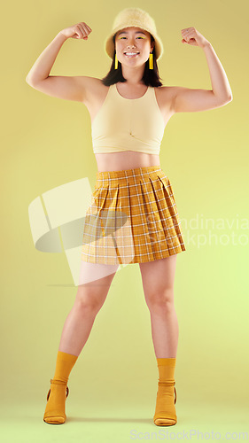 Image of Smile, empowerment and asian woman flexing arms, full body portrait of gen z model with trendy fashion win in studio. Feminism, power and strength, happy and strong girl isolated on yellow background