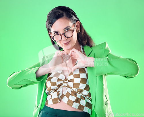 Image of Portrait, hands and heart with a woman on a green background in studio for love, romance or health. Social media, emoji and affection with a trendy person posing or making a hand sign for style