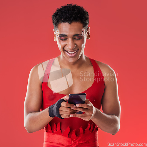 Image of Fashion, phone and gay man on social media in studio on a red background for communication. Mobile, transgender and a happy lgbt person looking at an internet meme while fashionable on a backdrop