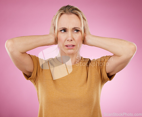 Image of Loud, studio and woman closing her ears in a studio for noise distraction, sound or complaint. Upset, mad and annoyed female model with a hands on her head for cover isolated by a pink background.