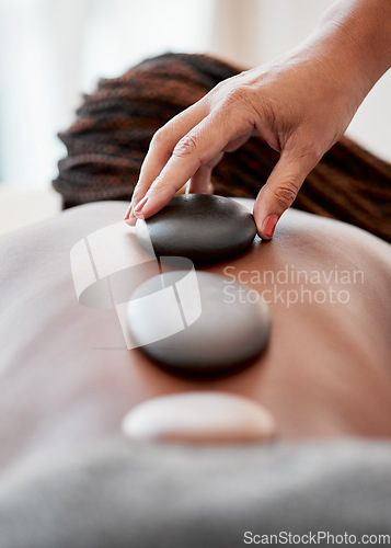 Image of Black woman, hands and rock on back in spa treatment for relaxation, stress relief or massage at resort. Hand of masseuse applying rocks to African American female in physical therapy for wellness