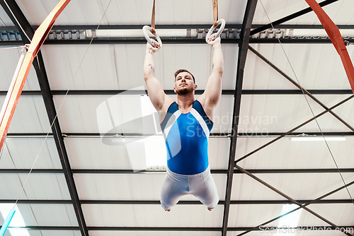 Image of Man, acrobat and gymnastics swinging on rings in fitness for practice, training or workout at gym. Professional male gymnast hanging on ring circles for athletics, acrobatics or strength exercise