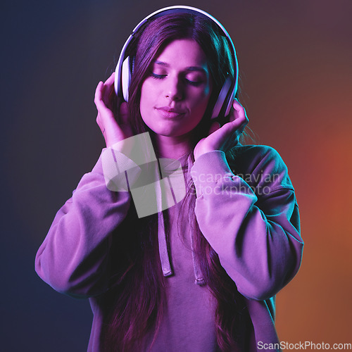 Image of Music, neon and gen z with a woman in studio listening to the radio for freedom on a wall background. Cyberpunk, headphones and streaming audio with an attractive young female hearing her best song