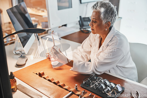 Image of Senior optometrist woman, glasses and design for focus, vision or frame planning at desk in clinic. Elderly optician, spectacle designer and eye care in workplace for fashion, small business and goal