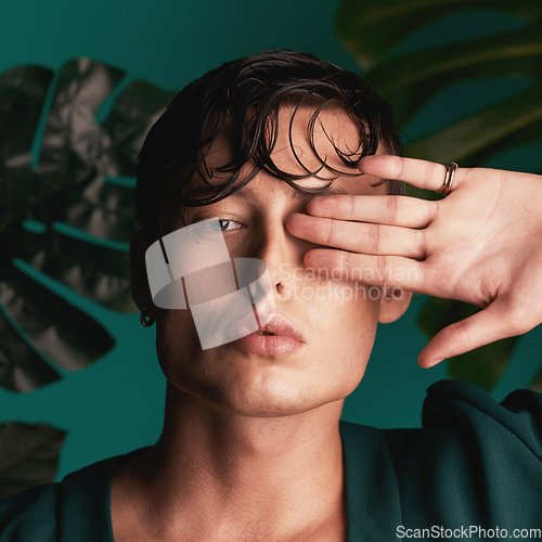 Image of Gen z, man and portrait of a male model with hand beauty and fashion face. Isolated, green background and studio of a young person with Monstera plants for organic skincare and eco friendly style