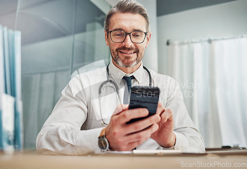 Image of Healthcare, smile and doctor with smartphone at desk for wellness research, medical app and online consulting. Hospital, clinic and happy man with phone for internet, communication and telehealth