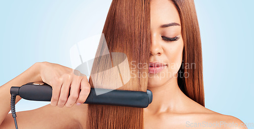 Image of Face, beauty and woman with hair straightener in studio isolated on a blue background. Haircare, wellness and young female model with flat iron for salon treatment hairstyle, aesthetic or balayage.