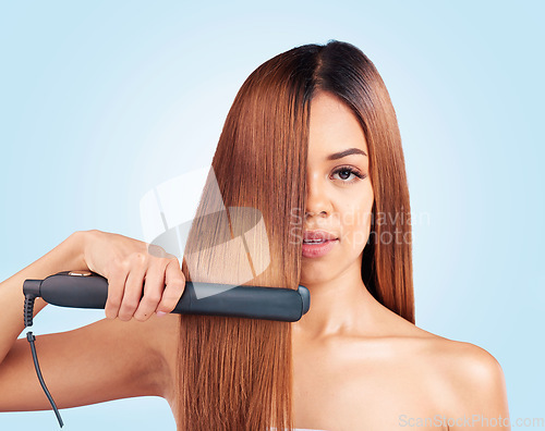 Image of Face portrait, beauty and woman with hair straightener in studio isolated on a blue background. Haircare, product and female model with flat iron for salon treatment, hairstyle aesthetic or balayage.