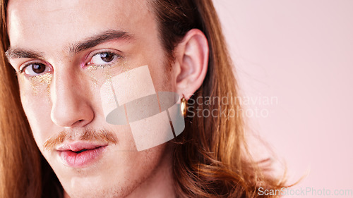 Image of Face portrait, beauty and man with makeup in studio isolated on a pink background. Gen z, lgbtq and gay, queer or homosexual young male model with gold glitter cosmetics for aesthetics and skincare.