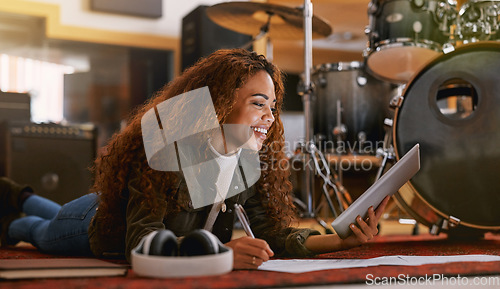 Image of Black woman, smile and tablet writing music in recording studio for audio track, content creation or development. Happy African female song writer smiling in lyrics holding touchscreen lying on floor