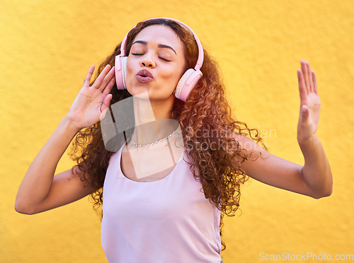 Image of Music, freedom and singing with a black woman listening to the radio outdoor on a yellow wall background. Headphones, energy and face with an attractive young female streaming audio sound for fun