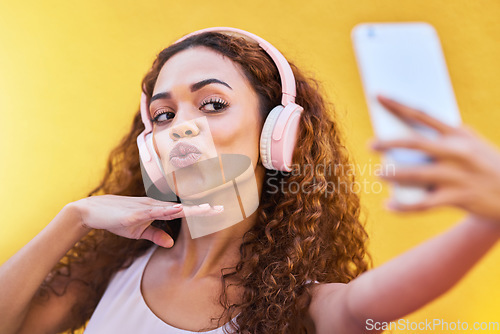 Image of Selfie, black woman and headphones for listening to music on yellow wall background. Face of happy gen z person pout lips with curly hair outdoor while streaming audio for influencer post in Colombia