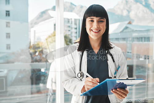 Image of Woman, doctor and portrait smile writing on clipboard by window for healthcare planning, strategy or notes. Female medical expert smiling with paperwork, prescription or medicare details at hospital