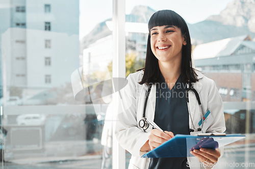 Image of Woman, doctor and smile writing on clipboard by window for healthcare planning, strategy or notes. Happy female medical expert smiling with paperwork, prescription or medicare details at hospital