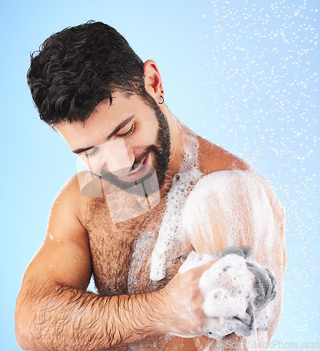 Image of Body, shower and man with sponge, soap and water splash in studio for wellness, hygiene and grooming. Skincare, cleaning and happy male with foam, bathroom cosmetics and washing on blue background