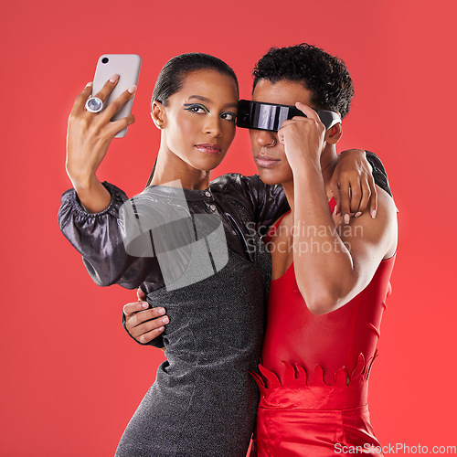 Image of Selfie, fashion and funky people isolated on red background for queer, creative gen z and cyberpunk aesthetic. Futuristic glasses, profile picture and beauty couple of friends, model or youth makeup