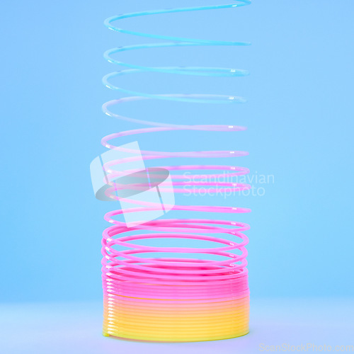 Image of Rainbow slinky toy, spring and plastic product in studio isolated against a blue background mockup. Flexible toys, colorful spirals and childhood item stretched out for playing, having fun and games.