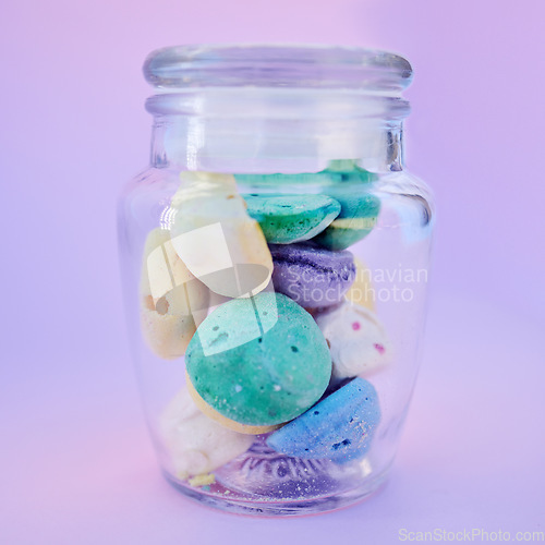 Image of Glass jar, beach stones or rocks on table in studio isolated on a purple background. Beauty, art and variety of colorful pebbles in bottle collected from sea or ocean coast for interior decoration.