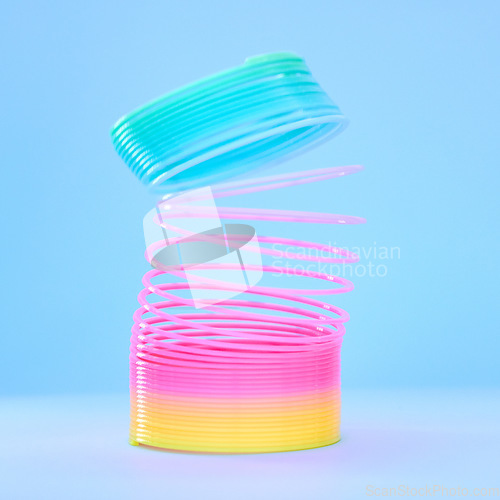 Image of Rainbow slinky toy, spring and plastic product in studio isolated against a blue background mockup. Flexible toys, colorful spirals and childhood item stretched out for playing, having fun and games.