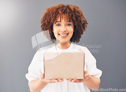 Image of Portrait, box and delivery with a black woman courier holding cardboard in studio on a gray background. Stock, supply chain and shipping with an attractive young female indoor to deliver goods