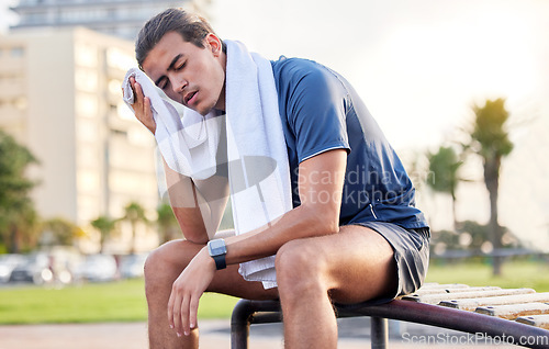 Image of Fitness, exercise and tired man with a towel on park bench to relax or rest after running for cardio. Sports person with fatigue and sweating outdoor post workout or training for health and wellness