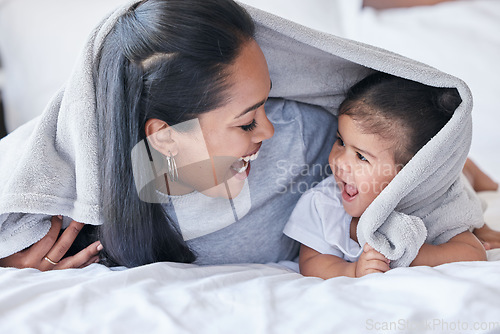 Image of Mother, parent and baby playing or bonding in a bed with blanket laughing being funny together in a bedroom or room. Mom, kid and single mum in a home or house with little daughter or child