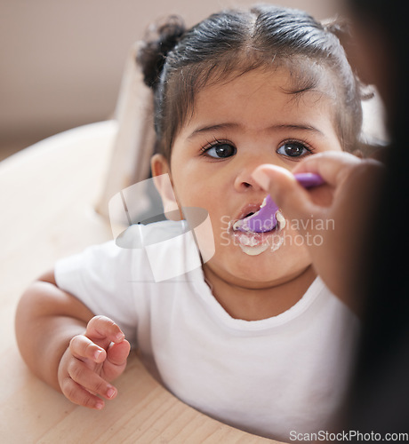 Image of Baby, food and hand feeding with spoon while eating for nutrition, development and growth in a chair. Face of girl toddler or child having breakfast, lunch or dinner while hungry in family home