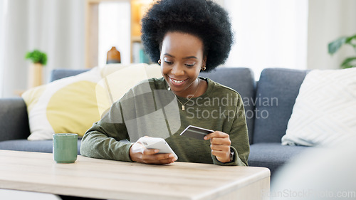 Image of Young black woman shopping online using her phone and bank credit card in a bright living room. Banking and managing assets and finance using convenient wireless technology from the comfort of home