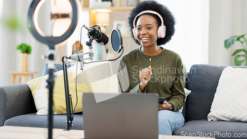 Image of Cool afro journalist using digital tablet, talking into microphone and hosting podcast or broadcasting news while wearing headphones. Excited young woman using technology to promote on air from home