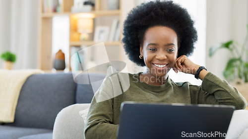 Image of Laughing afro woman using laptop to watch funny, comedy movies or videos. Smiling, happy woman with stylish, funky and cool hair sitting alone on home living room sofa, relaxing and using technology