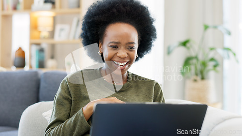 Image of Female with an afro enjoying a comedy movie on her laptop while eating a big bowl of popcorn at home. African woman laughing while watching funny movies on her couch. Young lady streaming online