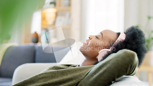 Image of Young woman listening to music while relaxing on a sofa at home. Carefree, cheerful and happy female wearing headphones while enjoying a podcast and favourite songs. Taking a break to rest in comfort