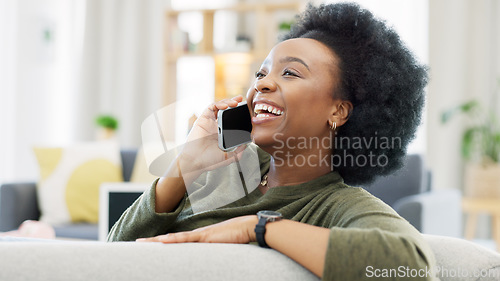 Image of Happy African woman talking on the phone while relaxing on her cozy sofa at home. Cheerful black female with afro laughing while having a pleasant and funny conversation with a friend on her mobile