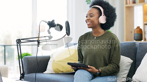 Image of Cool afro journalist using digital tablet, talking into microphone and hosting podcast or broadcasting news while wearing headphones. Excited young woman using technology to promote on air from home