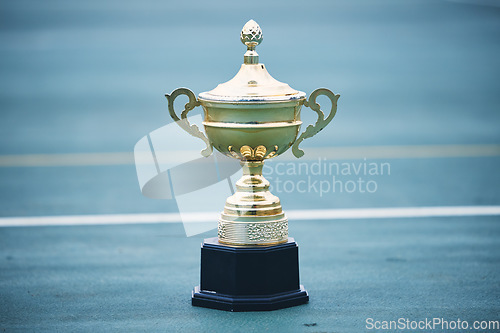 Image of Trophy, award and target with a sports cup on an empty court outdoor for the winner, champion or victor. Gold, goal and success with a prize on the floor outside at a stadium or arena for sport